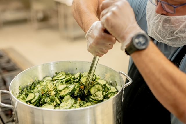 Hand-tossing cucumbers with spices in a large pot